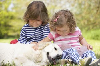 Two Children Petting Family Dog In Summer Field