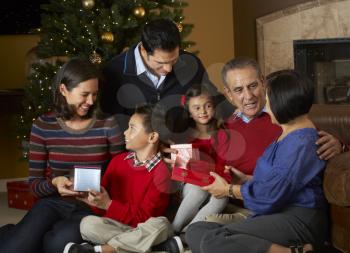 Multi Generation Family Opening Christmas Presents In Front Of Tree