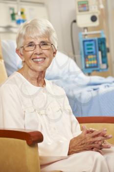Portrait Of Senior Female Patient Seated In Chair By Hospital Bed