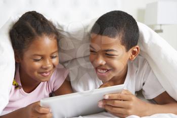 Two Children Using Digital Tablet Under Duvet