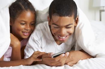 Two Children Using Mobile Phone Under Duvet