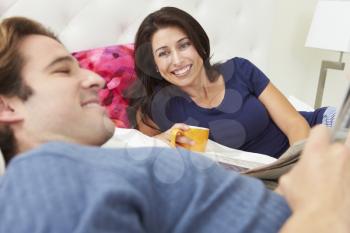 Couple Relaxing In Bed With Coffee And Newspaper