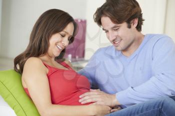 Man Relaxing On Sofa With Pregnant Wife At Home