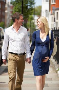 Couple With Pregnant Wife Walking Along Urban Sidewalk