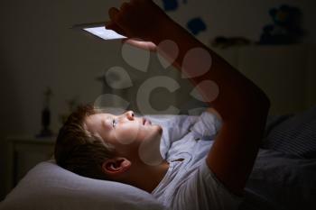 Boy Looking At Digital Tablet In Bed At Night