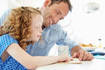 Father Helping Daughter With Homework In Kitchen