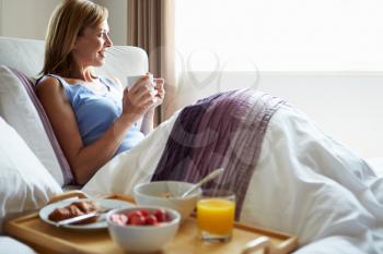 Middle Aged Relaxing In Bed With Hot Drink And Breakfast