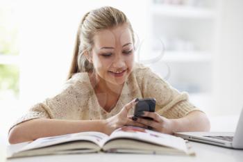Teenage Girl Sending Text Message Whilst Studying On Laptop