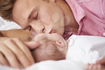 Father Kissing Baby Girl As They Lie In Bed Together