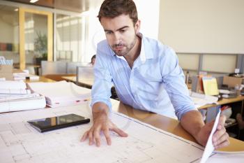 Male Architect With Digital Tablet Studying Plans In Office