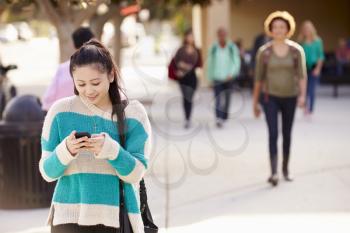 Female Student Walking To High School Using Mobile Phone