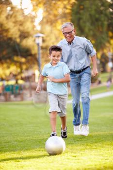 Grandfather Playing Football With Grandson In Park