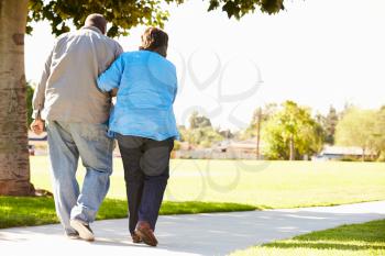 Senior Woman Helping Husband As They Walk In Park Together