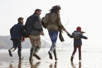 Rear View Of Family Running Along Winter Beach