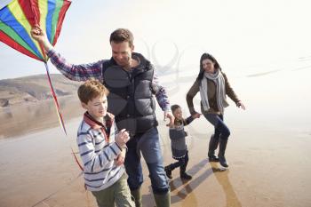 Family Running Along Winter Beach Flying Kite