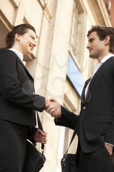 Businessman and business woman shaking hands outside building