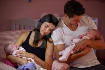 Tired Parents Cuddling Twin Baby Daughters In Nursery