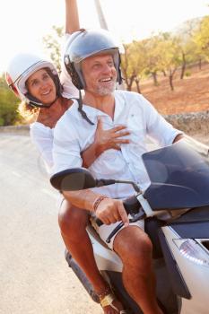 Mature Couple Riding Motor Scooter Along Country Road
