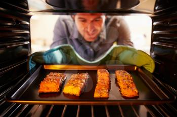 Man Putting Salmon Fillets Into Oven To Cook