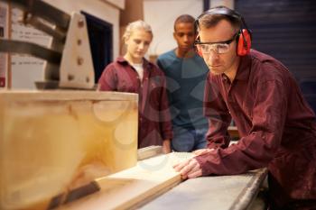 Carpenter With Apprentices Using Circular Saw In Workshop