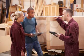 Carpenter With Apprentices Building Furniture In Workshop