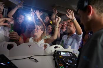 People Dancing In Nightclub With DJ In Foreground