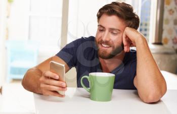 Young Man Drinking Coffee And Using Mobile Phone At Home