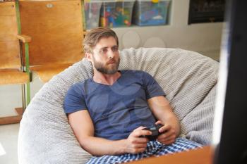 Man Wearing Pajamas Sitting In Chair And Playing Video Game