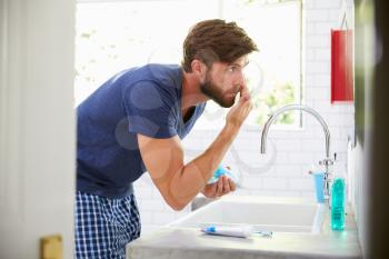 Man In Pajamas Putting On Moisturizer In Bathroom