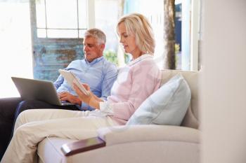 Mature Couple At Home In Lounge Using Digital Devices