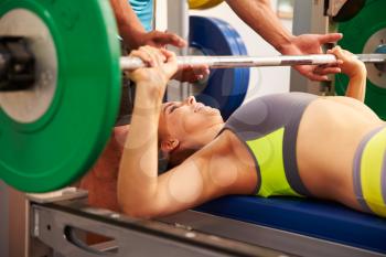Woman bench pressing weights with assistance of trainer