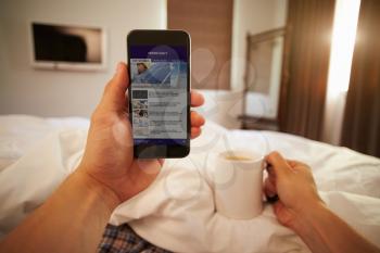 Man In Bed Looking At News Website On Mobile Phone