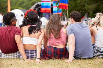 Young people sitting outdoors at a music festival, back view