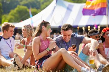 Friends sitting on grass using smartphone at music festival