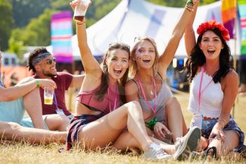 Friends sitting on the grass cheering at a music festival