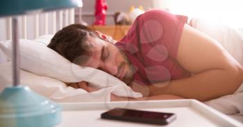 Man Asleep In Bed Using Alarm On Mobile Phone