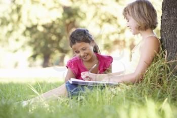 Two Young Girls Sketching In Countryside Leaning Against Tree