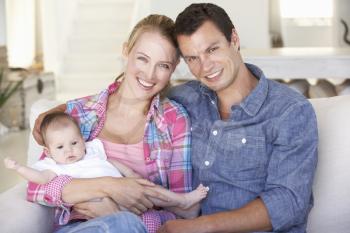 Young Family With Baby Relaxing On Sofa At Home
