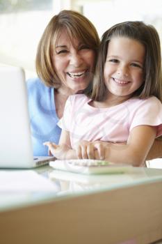 Hispanic Grandmother Using Laptop And Calculator With Granddaughter