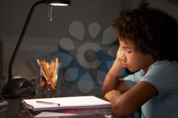 Unhappy Young Boy Studying At Desk In Bedroom In Evening