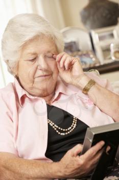 Unhappy Retired Senior Woman Sitting On Sofa At Home Looking At Photograph