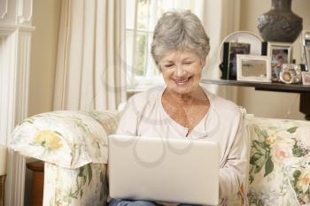 Retired Senior Woman Sitting On Sofa At Home Using Laptop