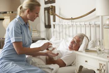 Nurse Giving Senior Male Medication In Bed At Home