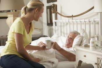Adult Daughter Giving Senior Male Parent Hot Drink In Bed At Home
