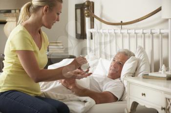 Adult Daughter Giving Senior Male Parent Medication In Bed At Home