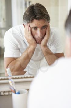 Unhappy Man Looking At Reflection In Bathroom Mirror