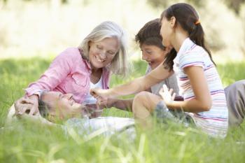 Grandparents With Grandchildren Relaxing In Summer Field