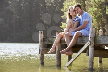 Young Romantic Couple Sitting On Wooden Jetty Looking Out Over Lake