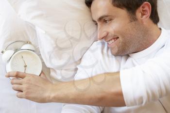Man Relaxing In Bed With Alarm Clock