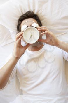 Man In Bed With Alarm Clock In Front Of Face